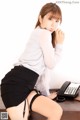 A woman in a white shirt and black skirt sitting at a desk.