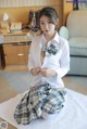 A woman in a white shirt and plaid skirt sitting on a bed.