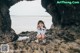 A little girl sitting on a rock by the ocean.