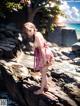 A woman in a pink dress standing on a rock by the water.