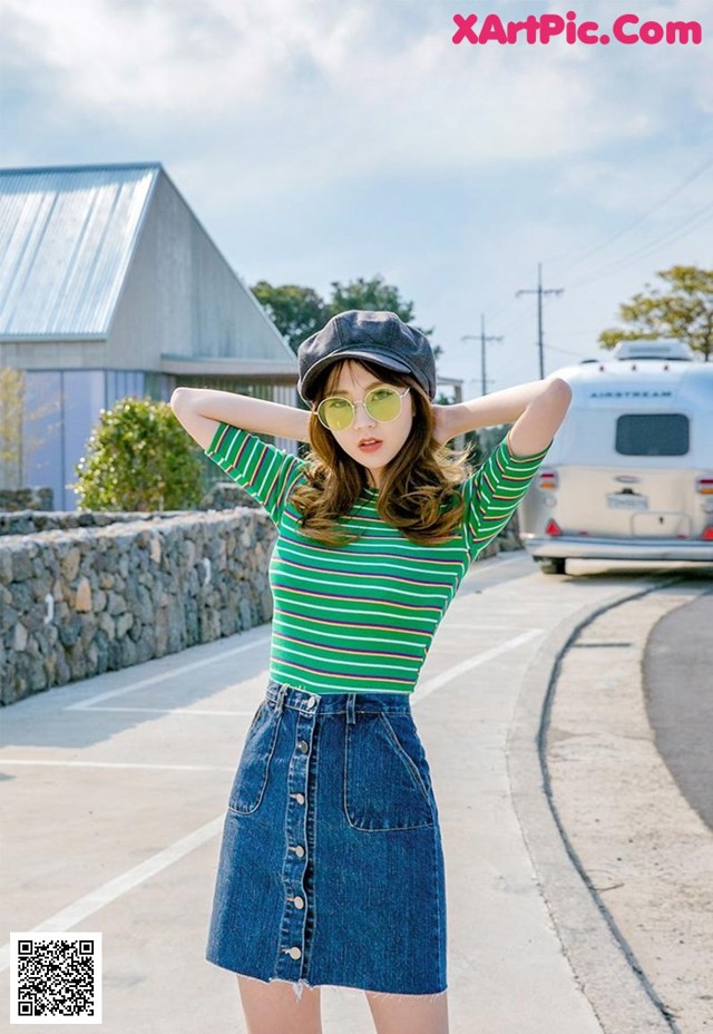 A woman wearing a green and white striped shirt and a denim skirt.