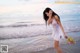 A woman in a white dress standing on the beach.