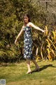 A woman in a blue and white floral dress standing in the grass.