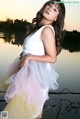 A woman in a white top and yellow skirt posing by a lake.