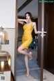 A woman in a yellow dress standing in front of a door.