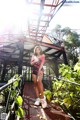 A woman in a pink shirt and black shorts posing on a bridge.
