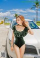 A woman in a green bodysuit standing next to a white car.