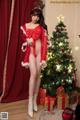 A woman in a santa outfit posing in front of a Christmas tree.