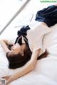 A woman laying on top of a bed in a white shirt and blue skirt.