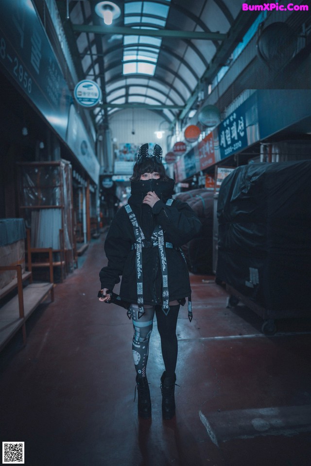 A woman wearing a black jacket and a black mask walking down a street.