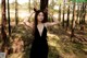 A woman in a black dress standing in the woods.