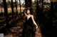 A woman in a black dress standing in the woods.