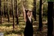 A woman in a black dress standing in the woods.