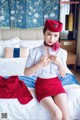 A woman in a red skirt and hat sitting on a bed.