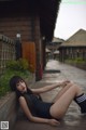 A woman in a black bathing suit laying on a wooden bench.