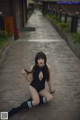 A woman in a black bodysuit sitting on a wooden walkway.