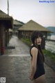 A woman in a black bathing suit standing on a wooden walkway.