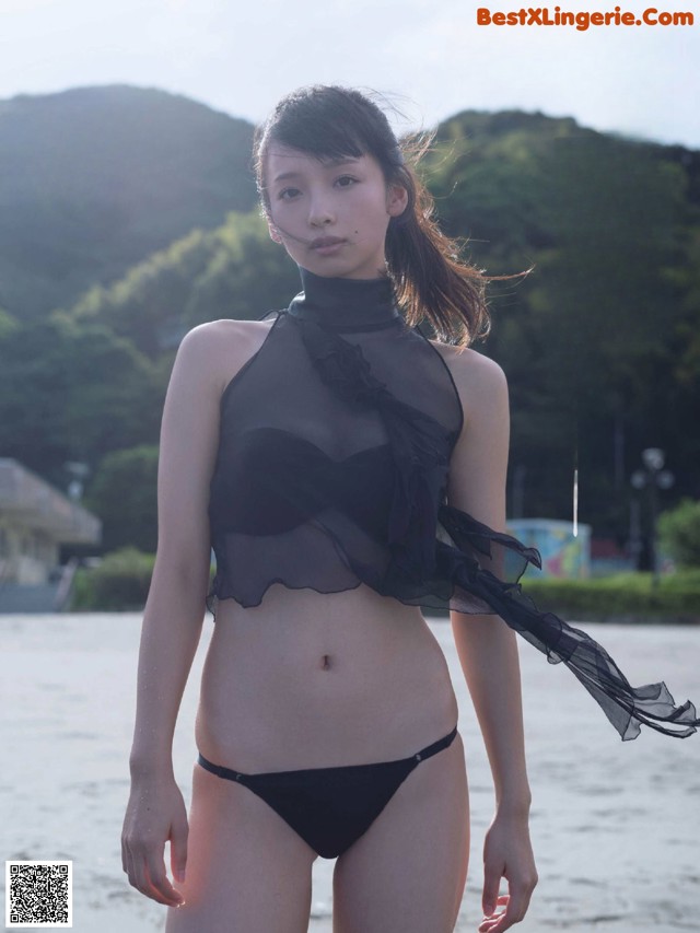 A woman in a black bikini standing on a beach.