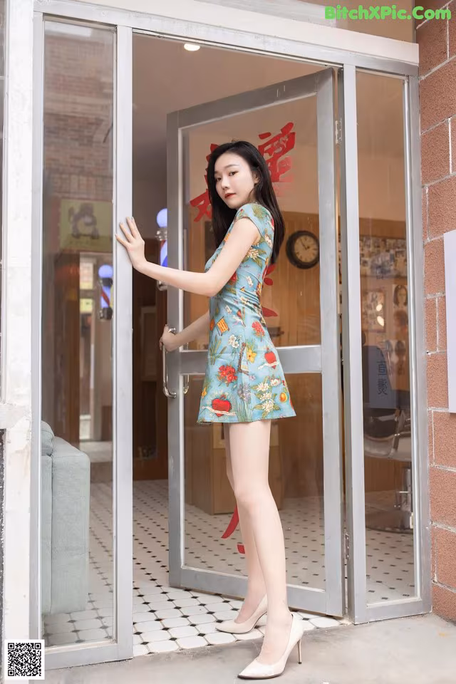 A woman in a blue dress standing in front of a glass door.