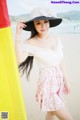 A woman in a white dress and a black hat on the beach.